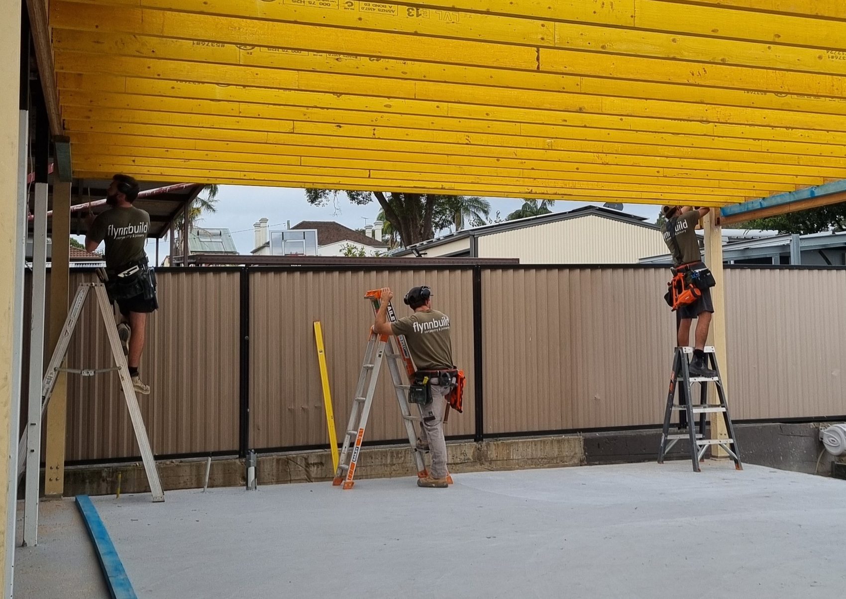 Flynnbuild crew installing roof framing beam on ladders